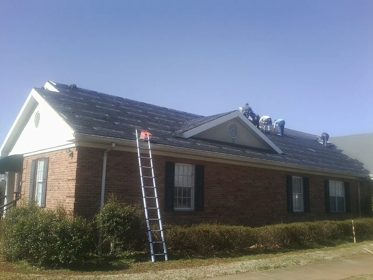 Crew tearing shingles off a brick ranch roof with a ladder set — Metal Roof Repair work by our crew in Wayne